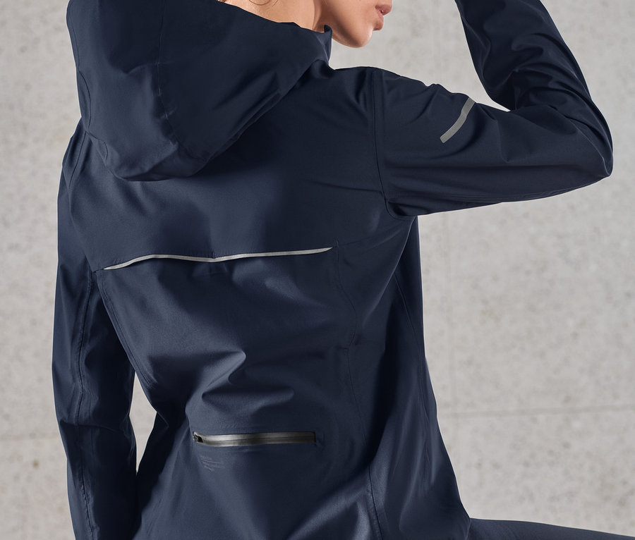 Femme essuyant son front, portant une veste de sport imperméable bleu foncé.