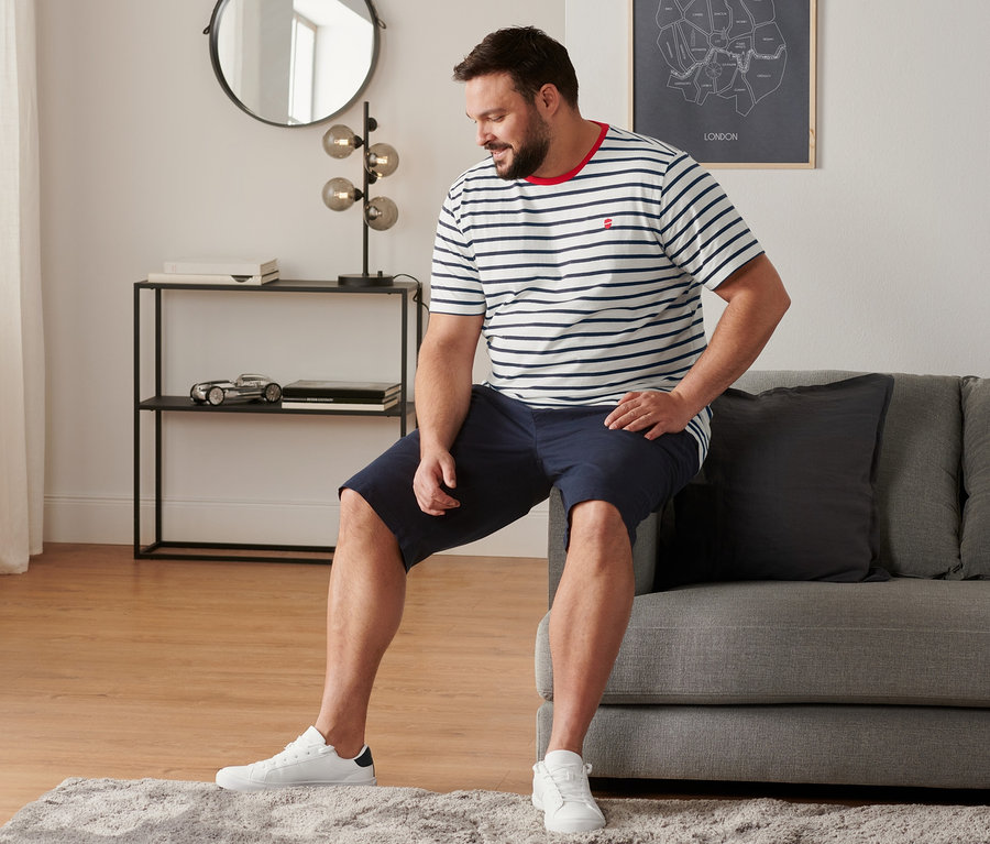 Homme assis sur un canapé portant des tennis, un short chino bleu marine et 2 t-shirts à encolure ronde rayés.