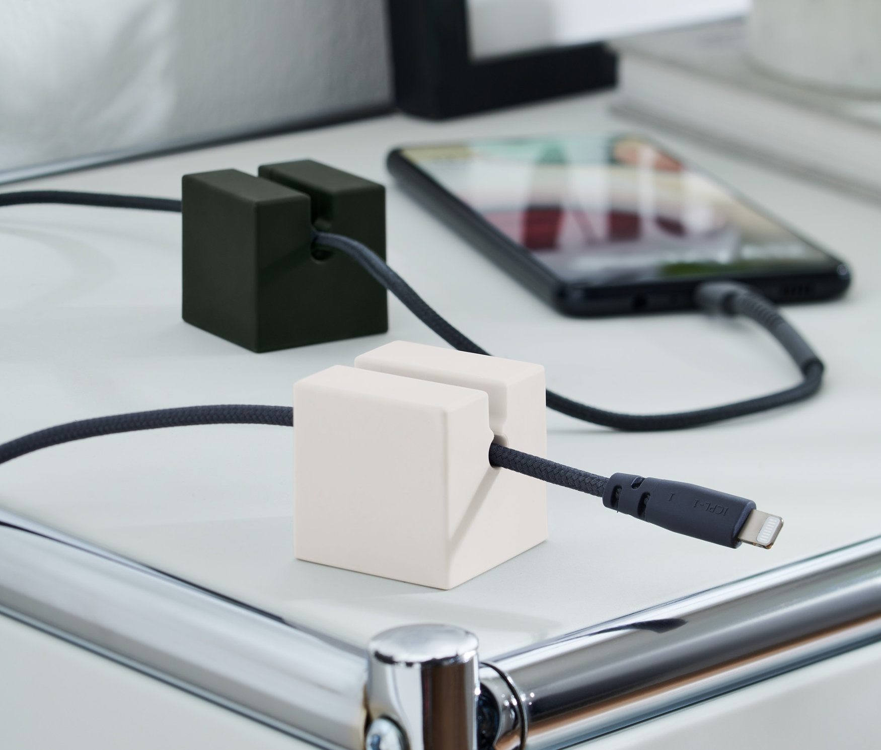 Un organisateur de câble de recharge, en 2 parties, maintient les câbles de recharge sur une table blanche. L'un est noir et l'autre blanc.