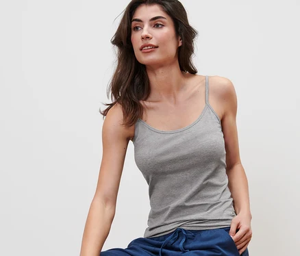 Femme assise sur un tabouret portant une chemisette spaghetti grise de 5 chemisettes spaghetti, blanches, noires, grises.