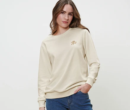 Une femme pose dans un sweatshirt crème avec broderie et un jean bleu.