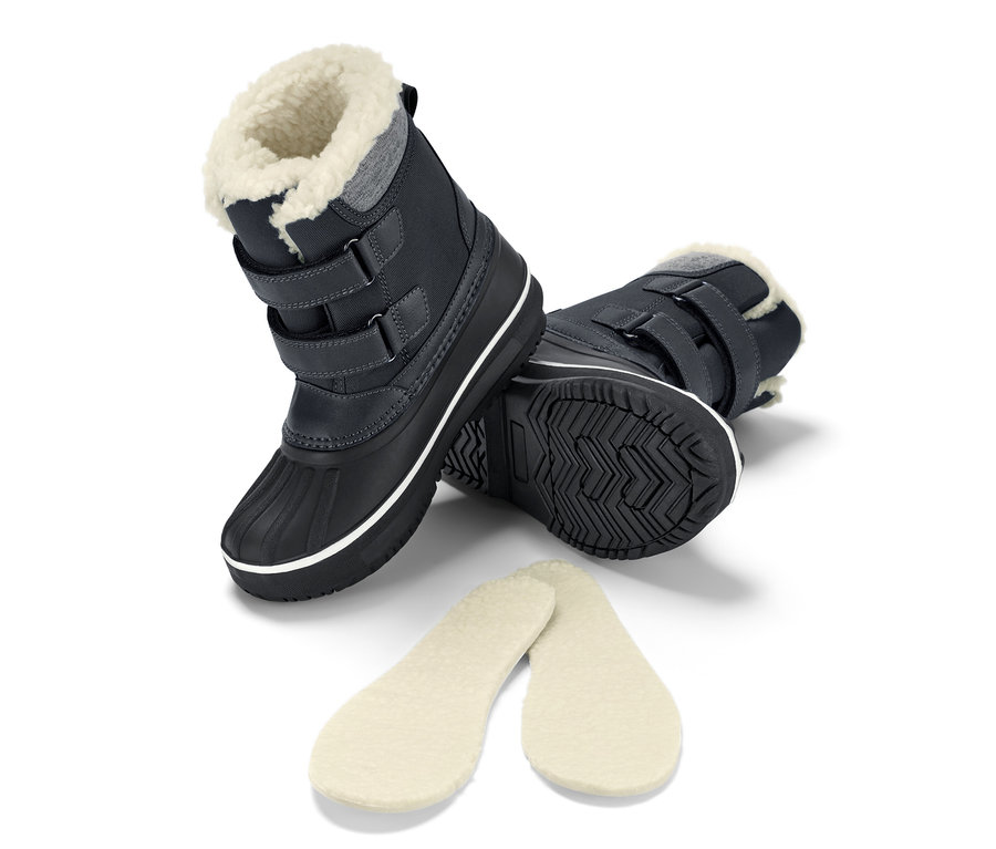 Bottes polyvalentes noires pour enfants posées sur le côté avec des semelles.