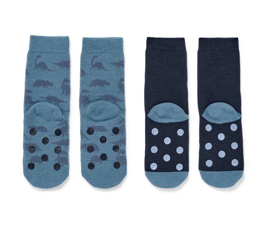 Deux paires de chaussettes antidérapantes pour enfant. Une paire bleue avec des dinosaures et des éléments antidérapants, l'autre bleu foncé avec des pois.