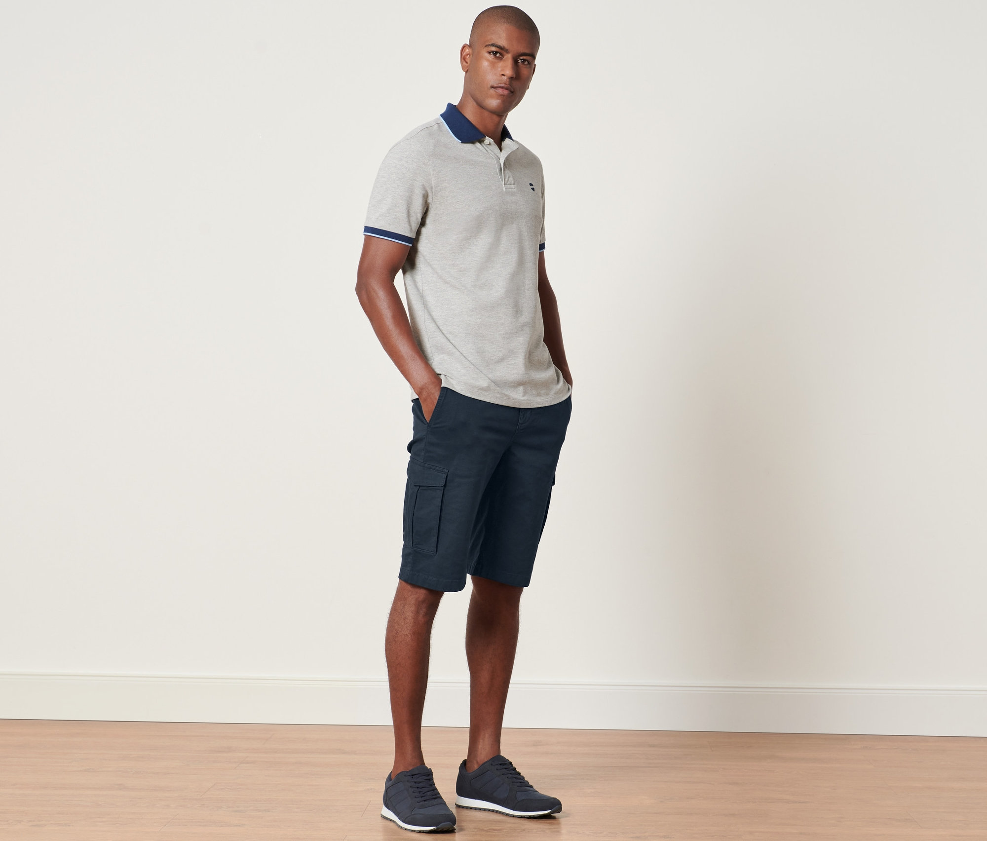 Un homme debout, les mains dans les poches d'un short cargo bleu marine.