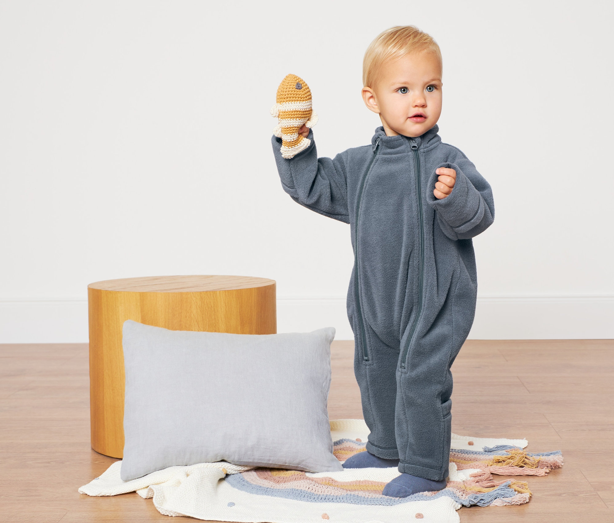 Un bébé vêtu d'une combinaison en polaire bleue tient un jouet.