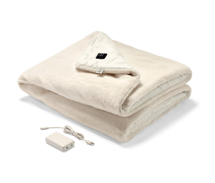 Un poncho chauffant à batterie crème plié avec un panneau de commande et une batterie visibles.