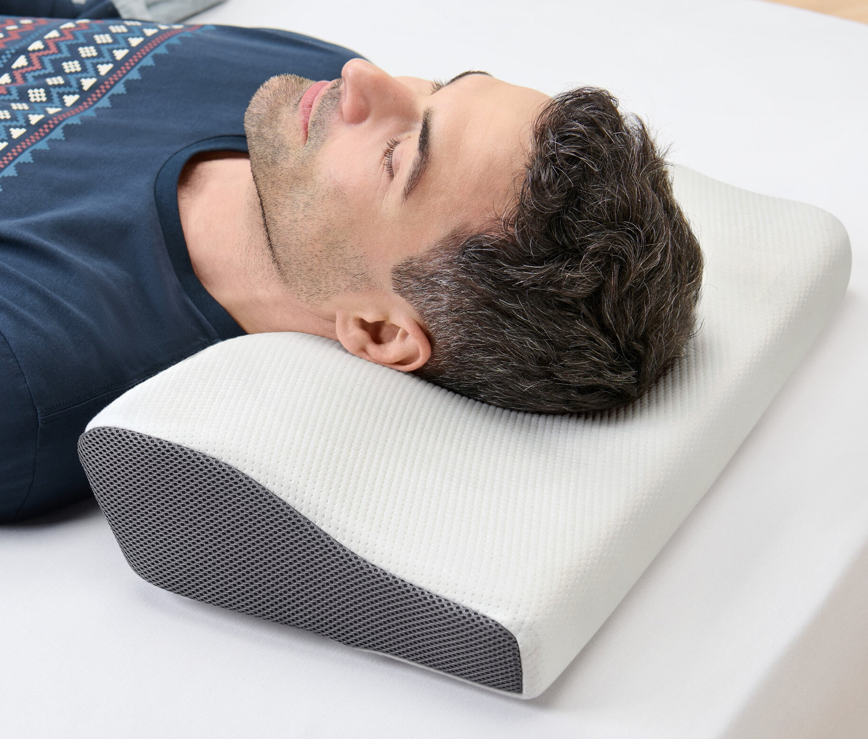 Un homme est allongé sur le côté sur un drap blanc, la tête posée sur un oreiller cervical.