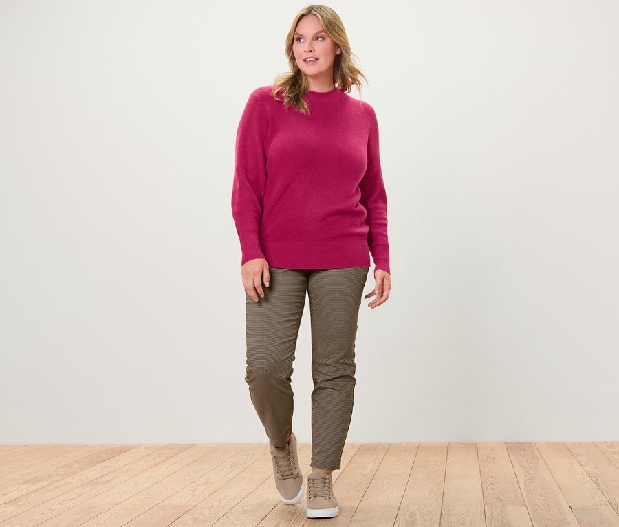 Une femme marche et porte un pull en maille fine rouge framboise et un pantalon stretch avec jacquard pied-de-poule.