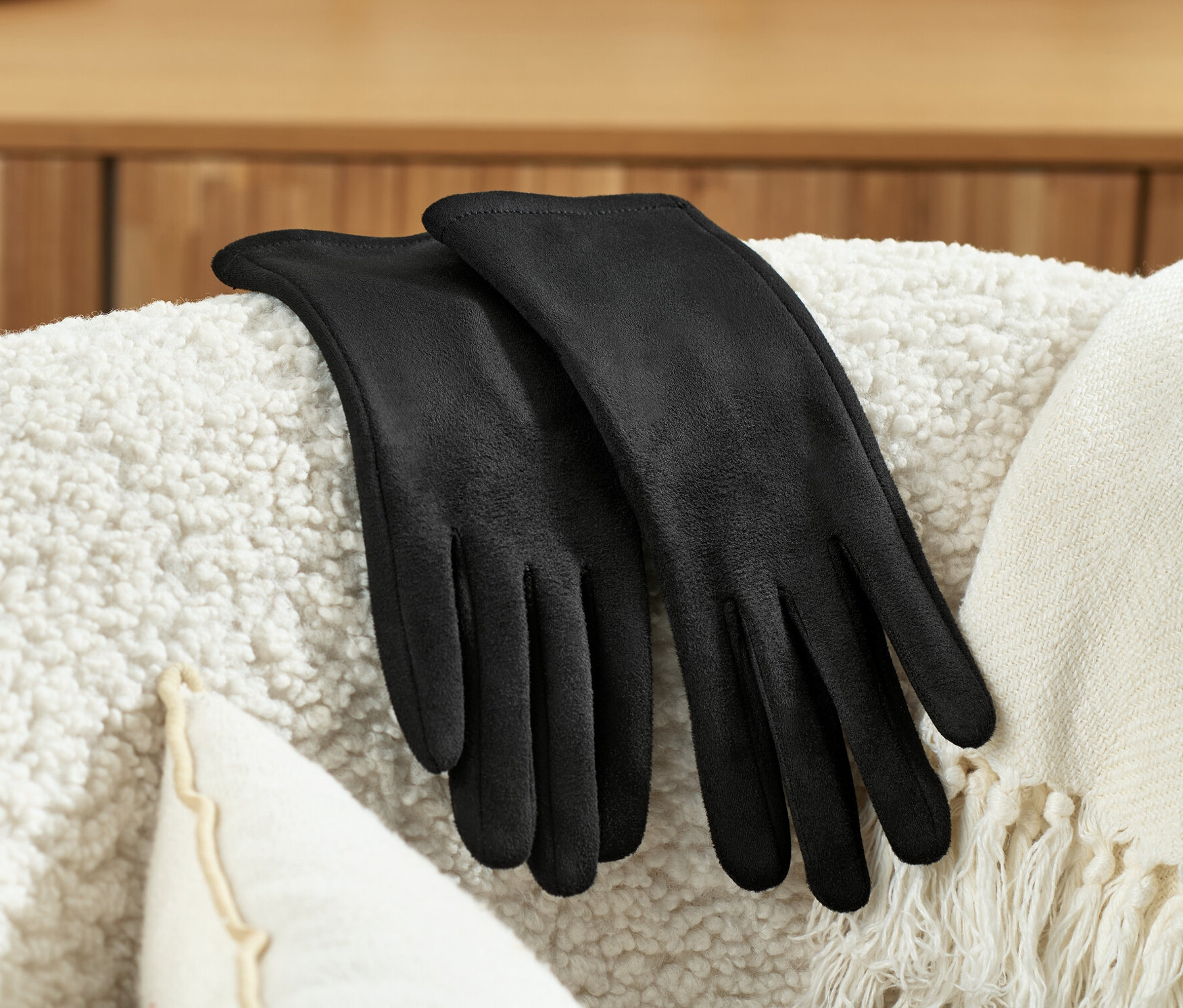 Des gants noirs aspect cuir velours sont posés sur un fauteuil blanc.