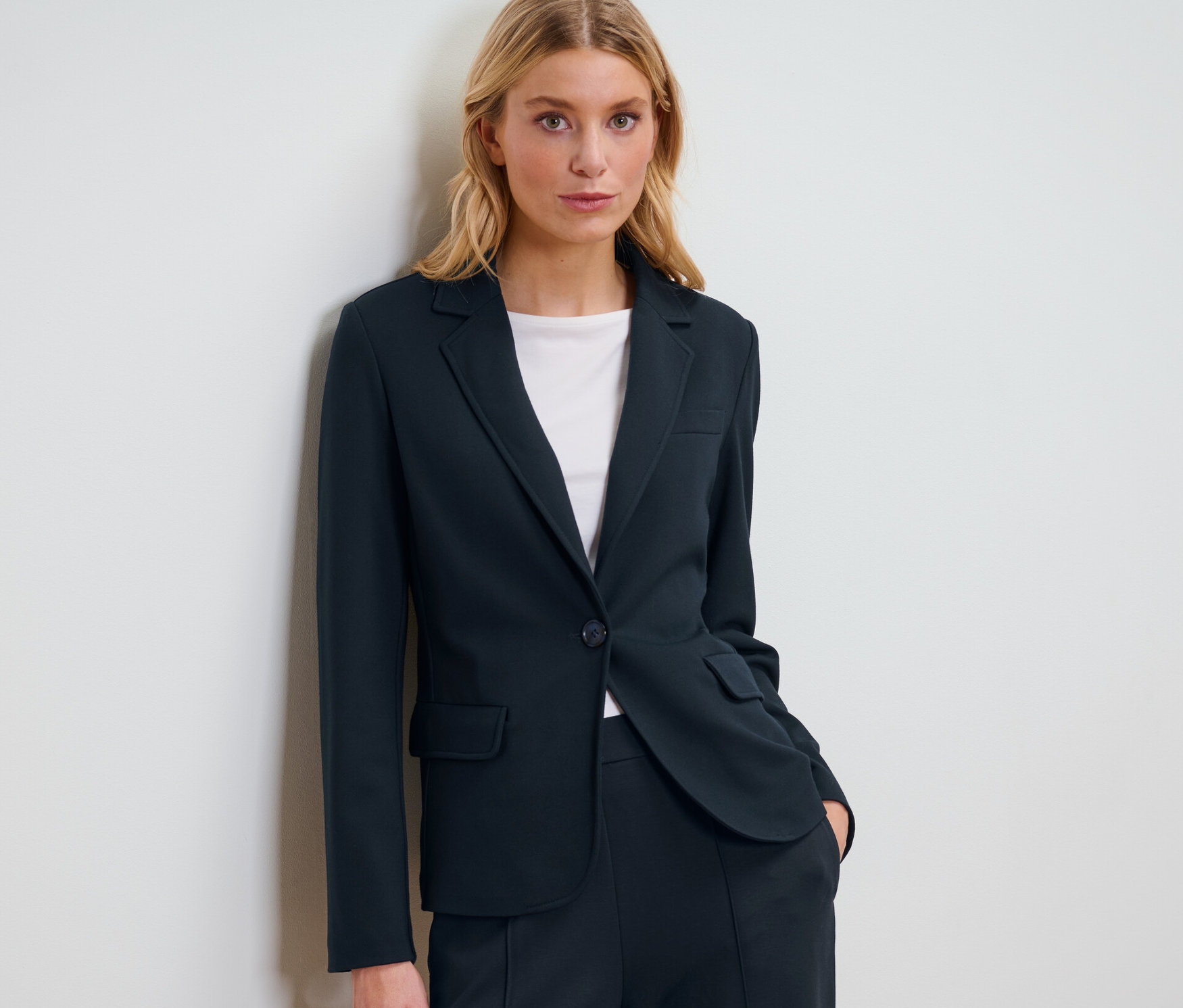 Une femme blonde pose en blazer en jersey bleu marine.