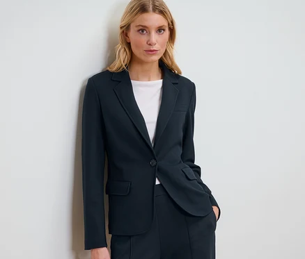 Une femme blonde pose en blazer en jersey bleu marine.