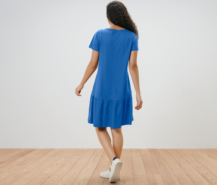 Une femme vue de dos porte une robe en jersey à volants bleu cobalt.