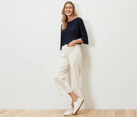 Femme posant en chemisier plissé, pantalon blanc et baskets.