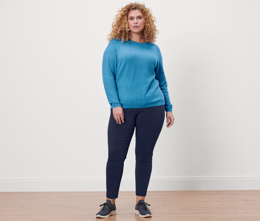 Une femme debout portant un pantalon stretch bleu foncé et un pullover en tricot bleu azur.