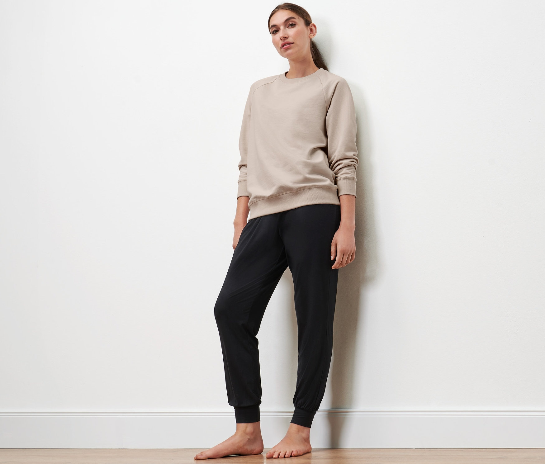 Une femme debout porte un sweat-shirt de yoga beige et un pantalon noir.