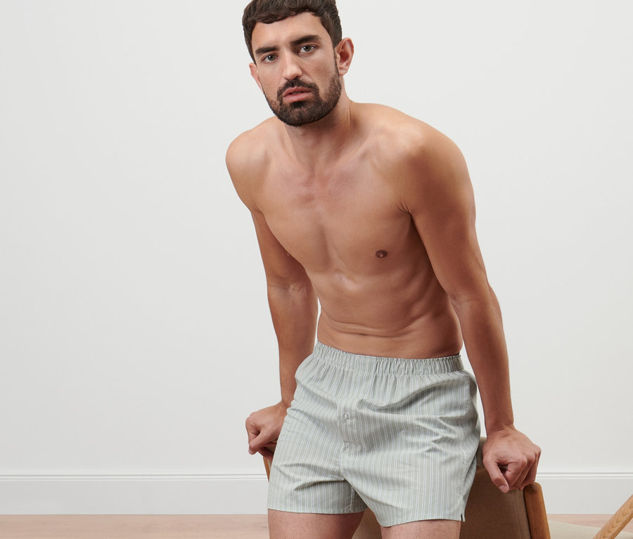Un homme appuyé sur une chaise porte 2 caleçons tissés.