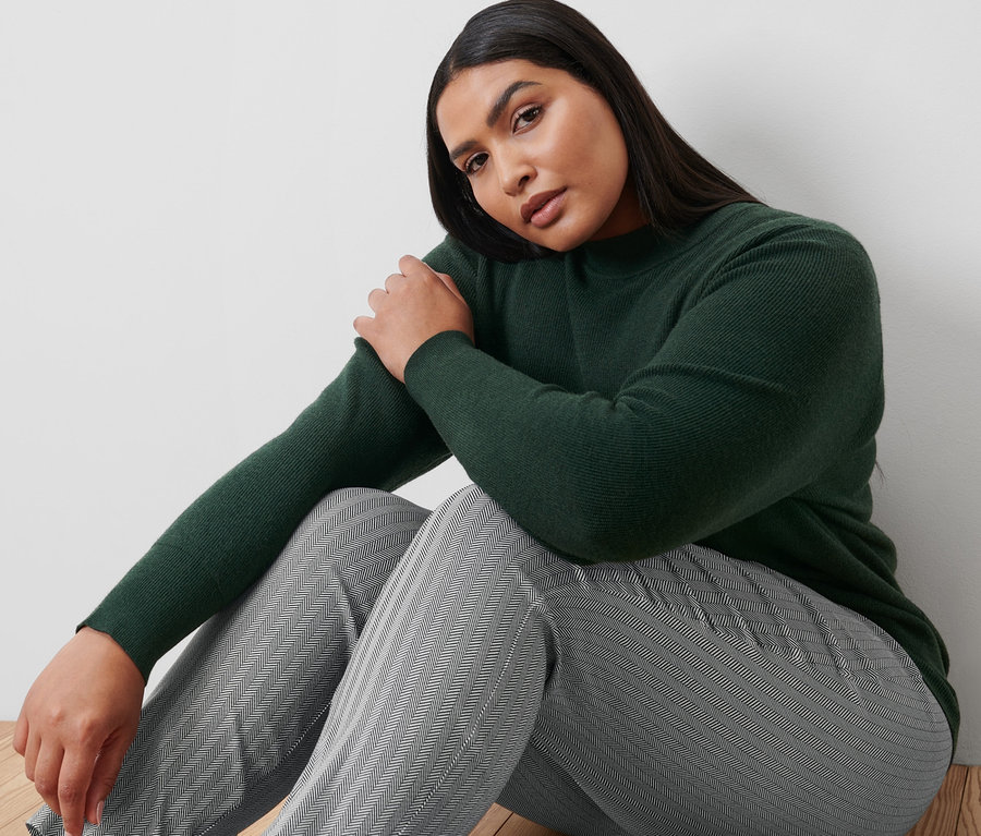 Une femme est assise par terre et porte un pantalon stretch imprimé et un pull en maille fine.