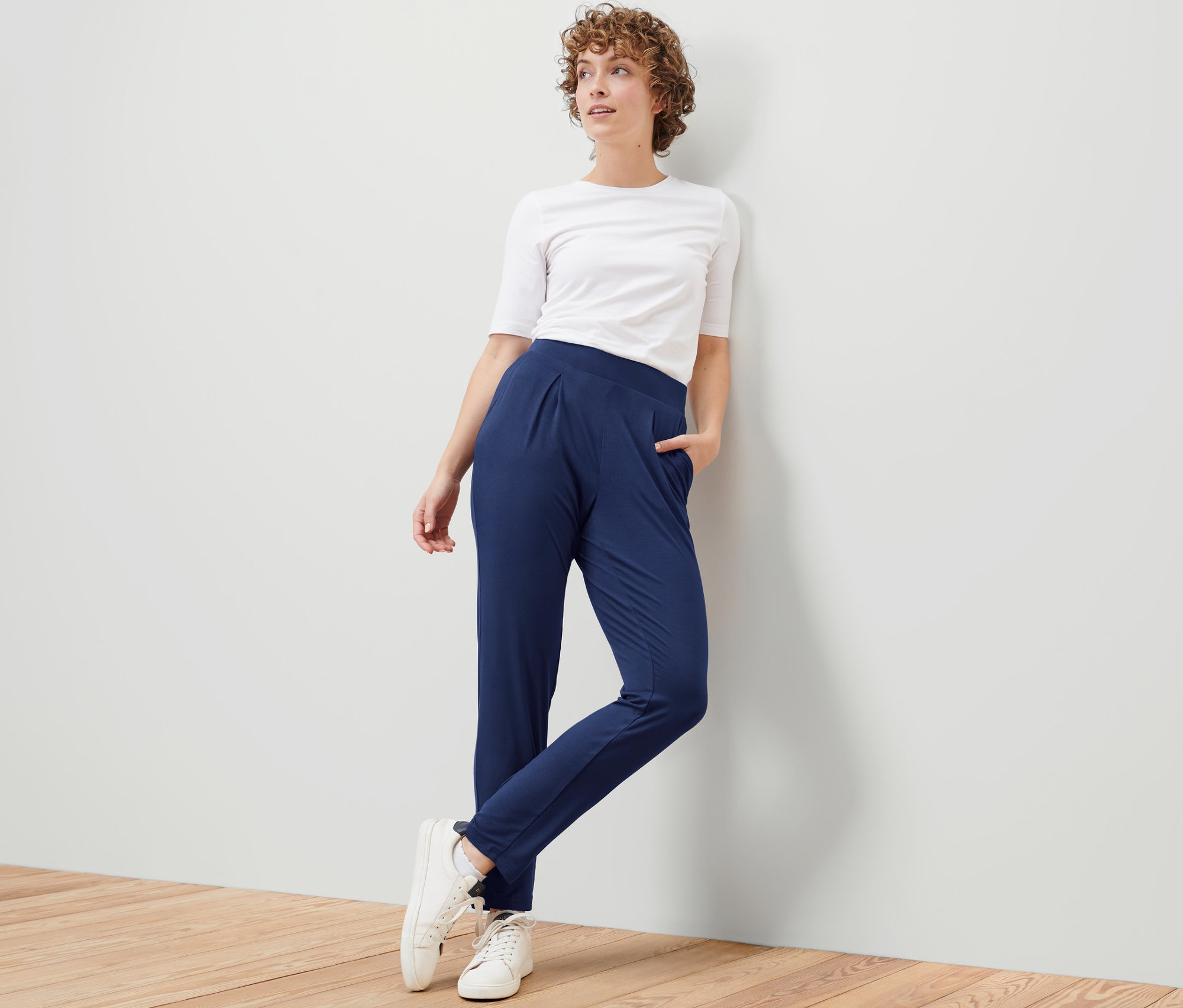Une femme appuyée contre un mur porte un pantalon en jersey bleu foncé.