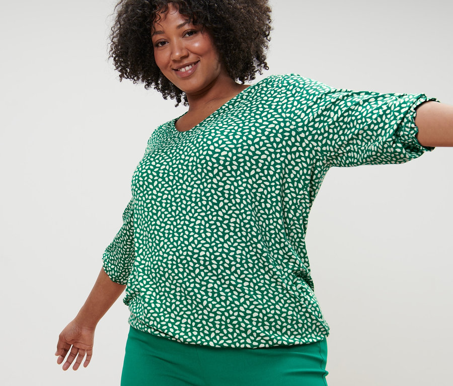 Femme posant en blouse imprimée verte et pantalon stretch vert.