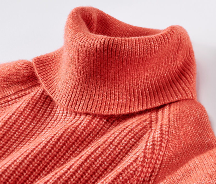 Gros plan d'un pull à col roulé en grosse maille orange.