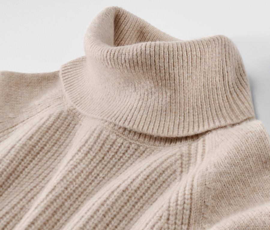 Gros plan d'un pull à col roulé en grosse maille beige.