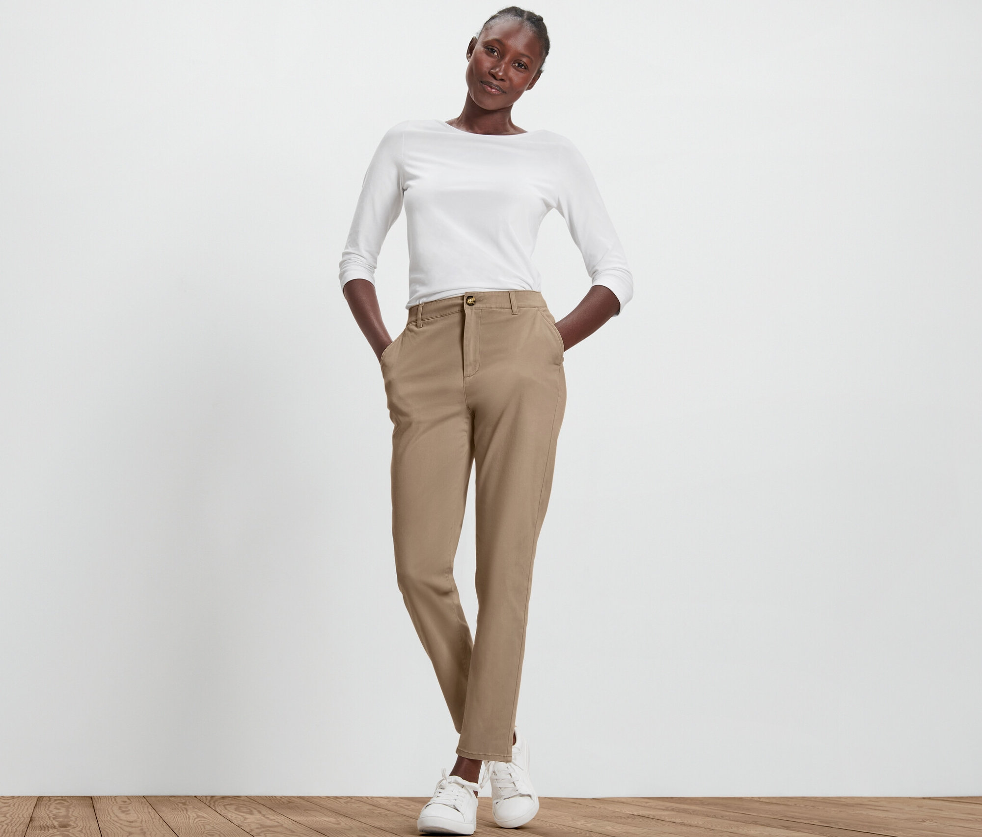 Femme posant en pantalon chino beige et haut blanc.