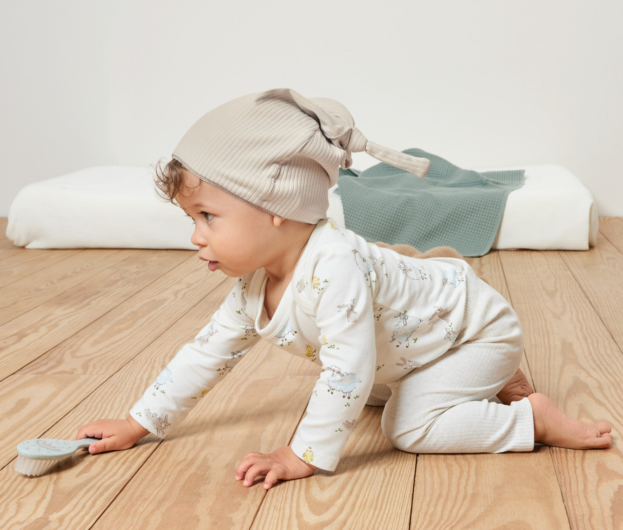 Bébé rampant sur un plancher en bois portant un bonnet en jersey beige.