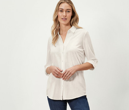 Une femme pose en chemisier en jersey piqué blanc crème et un jean bleu marine.