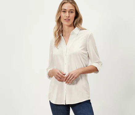 Une femme pose en chemisier en jersey piqué blanc crème et un jean bleu marine.