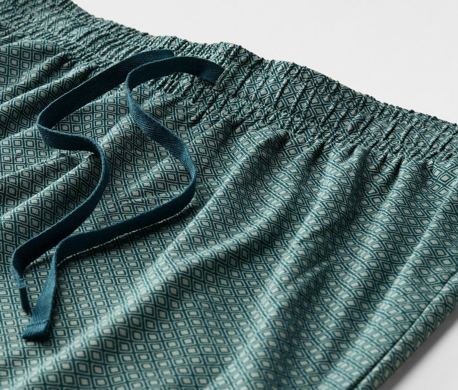 Gros plan d'un pantalon de pyjama vert à motifs avec une taille élastique et un cordon de serrage.