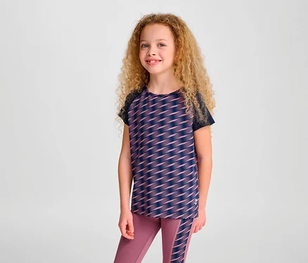 Une fille aux cheveux bouclés pose en T-shirt S/S HUMMEL HMLJR Mix et leggings.