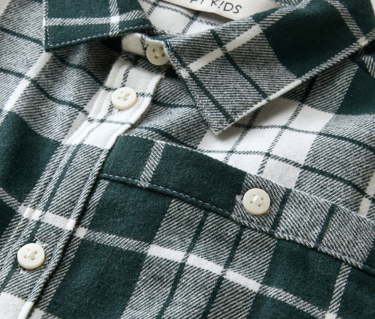 Détail d'une chemise à carreaux vert et blanc avec des boutons et un patch avec l'inscription Happy Kids.