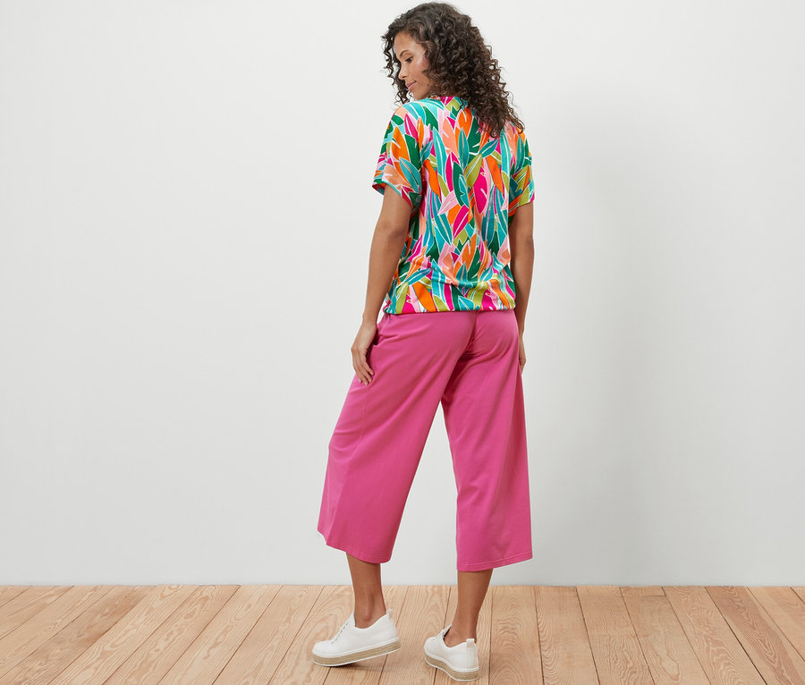 Femme vue de dos portant un chemisier à encolure dégagée à imprimé intégral et un pantalon rose.