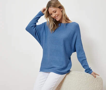 Femme assise portant un pull bleu en maille fine.