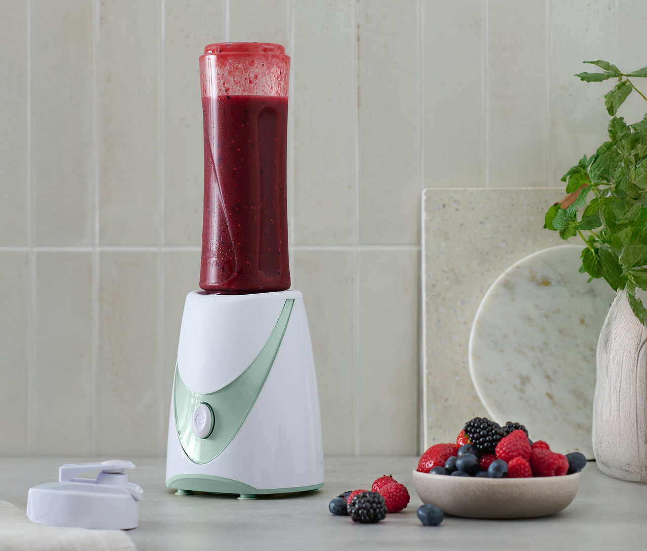 Un mini-blender à smoothie avec un smoothie prêt à l'emploi sur le dessus, à côté d'un bol de baies.