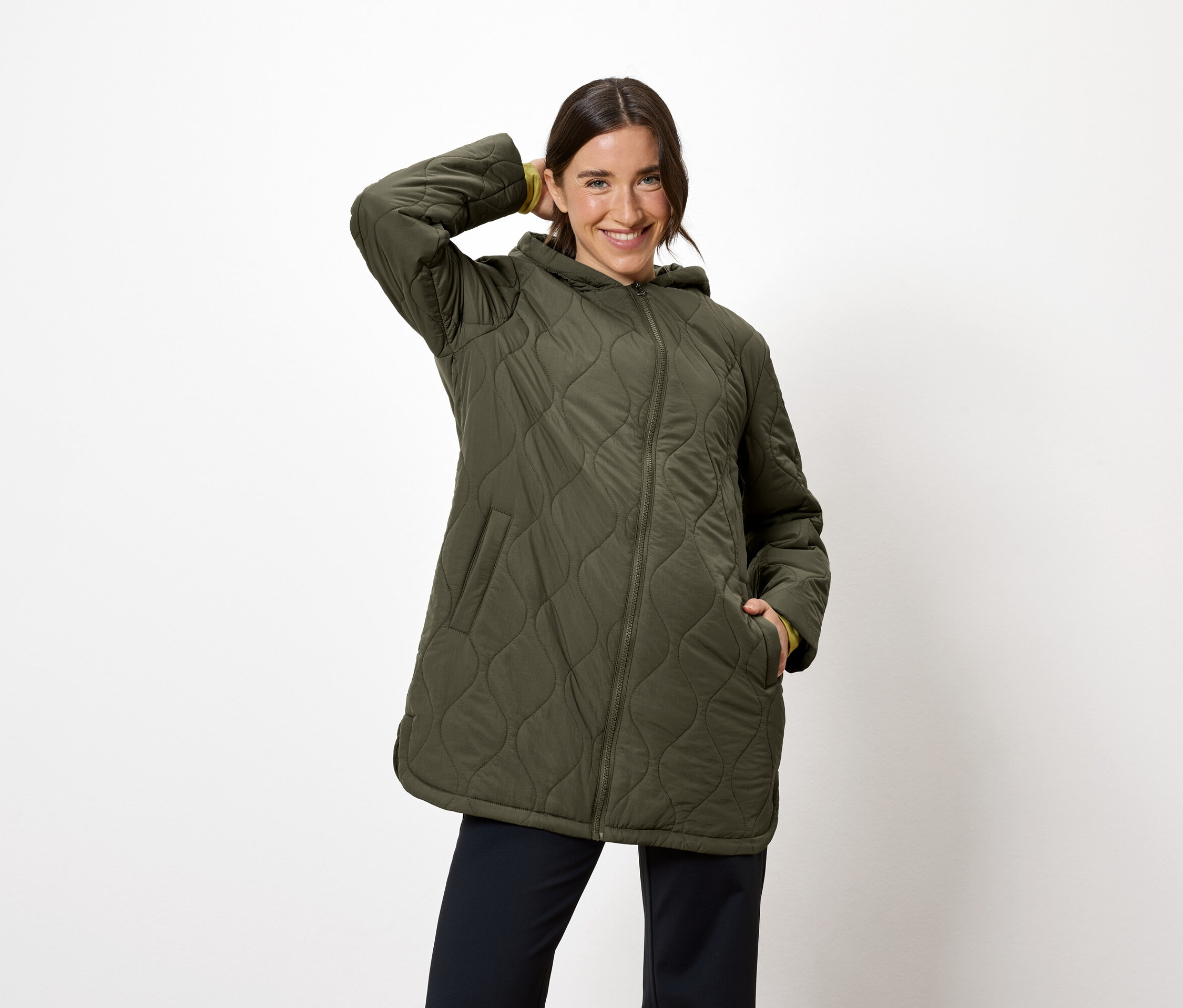 Femme posant dans une veste matelassée vert olive avec capuche et un pantalon bleu marine.