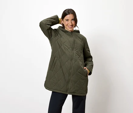 Femme posant dans une veste matelassée vert olive avec capuche et un pantalon bleu marine.
