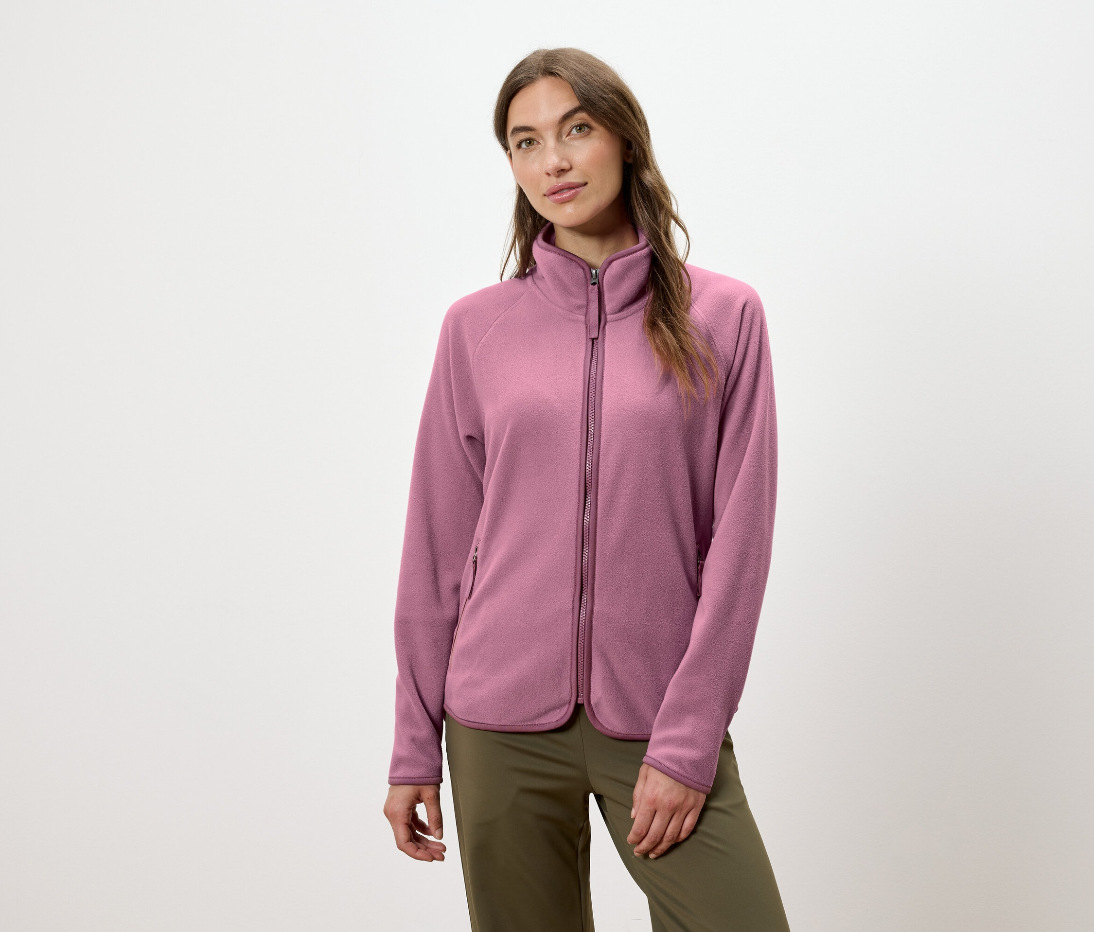 Une femme porte une veste en polaire rose zippée et un pantalon vert.