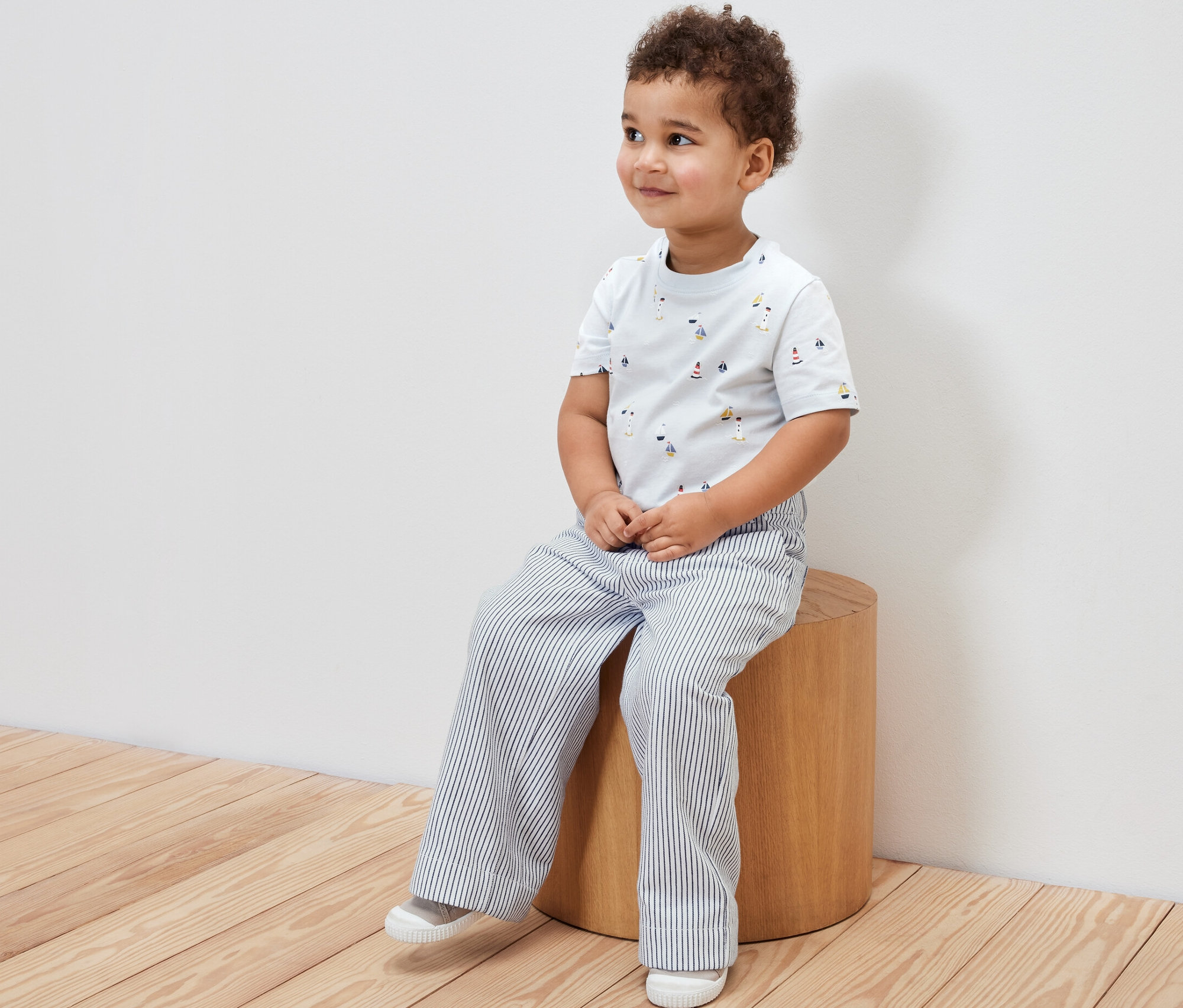 Un garçon est assis sur un tabouret et porte un pantalon tissé pour enfant et un t-shirt imprimé.