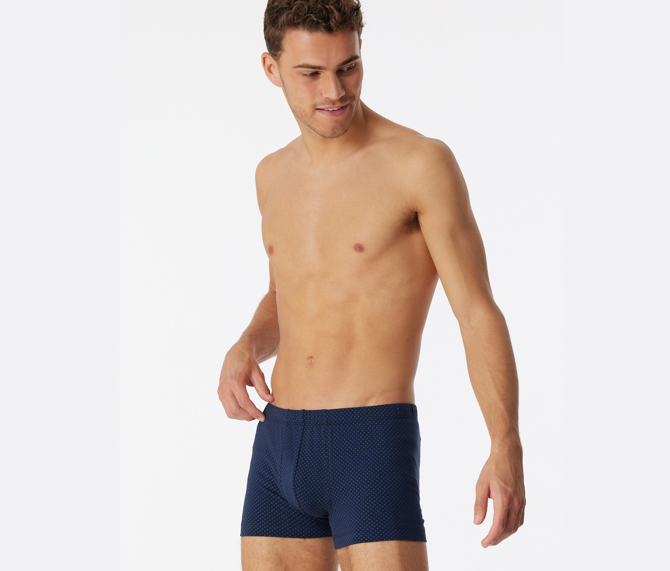 Homme regardant vers le bas et tenant le haut d'un short SCHIESSER bleu à imprimé intégral.