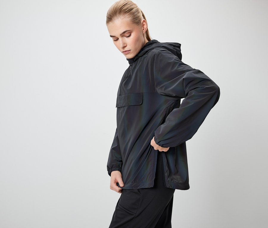 Une femme portant un anorak noir à capuche regarde vers le bas et tient l'anorak.