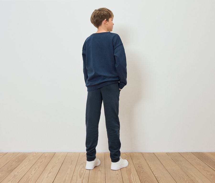Un garçon en sweat-shirt bleu et pantalon bleu, dos à la caméra.