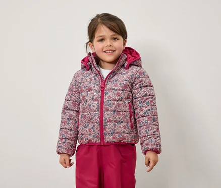 Une fille porte une veste à fleurs et un pantalon rose.