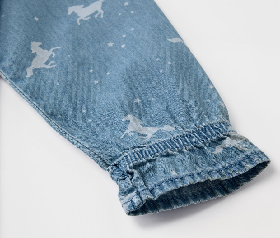 Détail de la manche d'une robe en jean pour enfant avec des motifs de chevaux et d'étoiles.