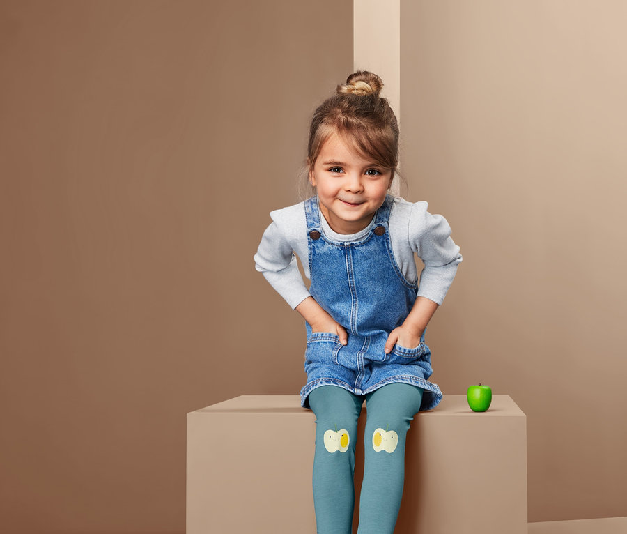 Une fille est assise et porte une robe en jean et 2 leggings avec des patchs.