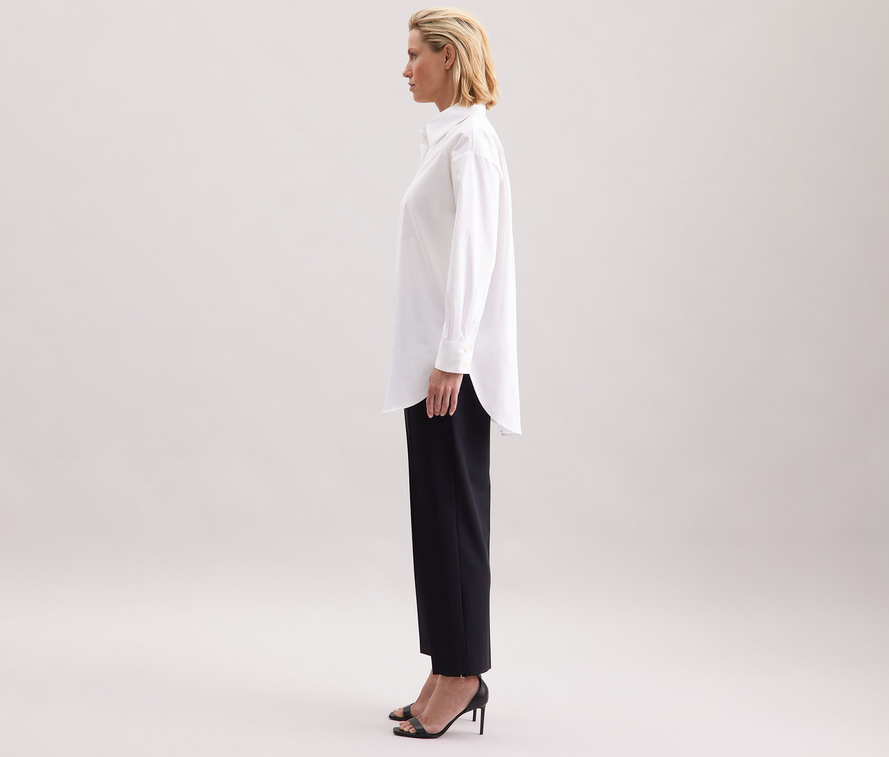Femme portant une blouse-chemise blanche grande taille Seidensticker, un pantalon noir et des chaussures à talons hauts.