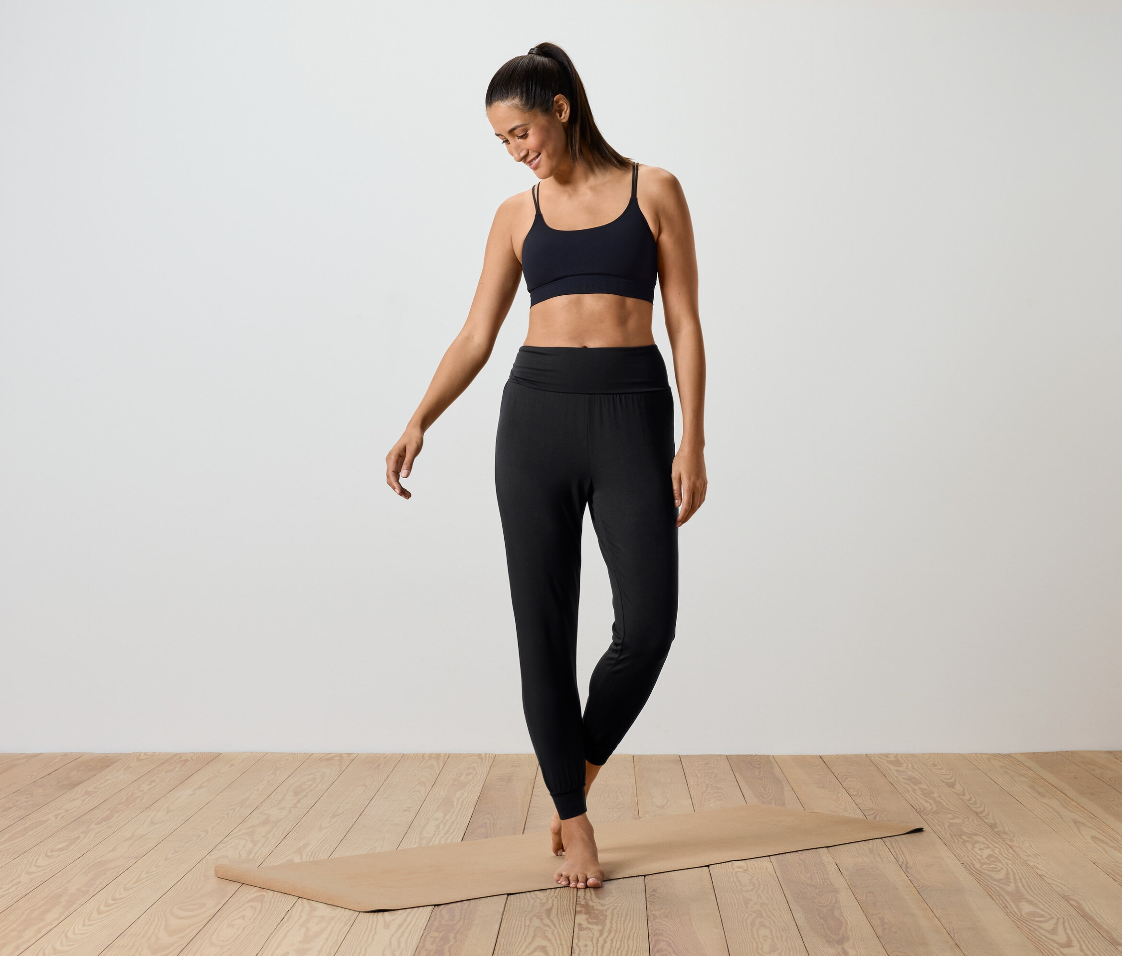 Une femme debout sur un tapis de yoga portant un soutien-gorge de sport noir et un legging noir.