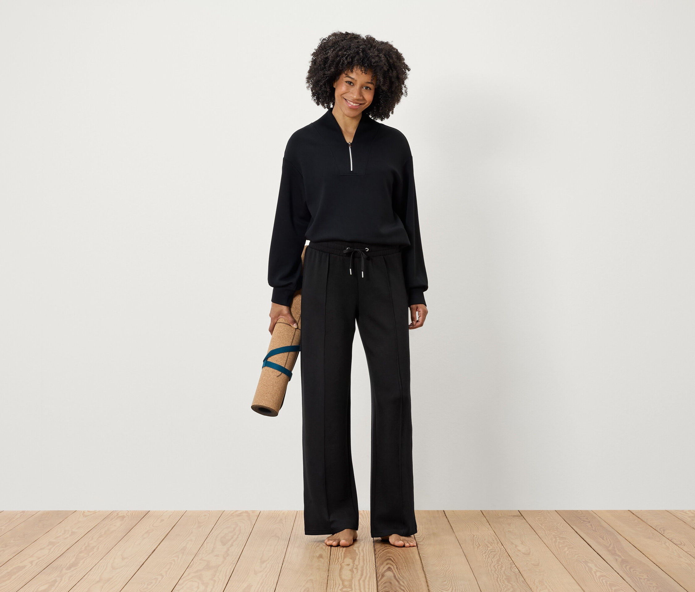 Femme tenant un tapis de yoga dans des vêtements noirs.