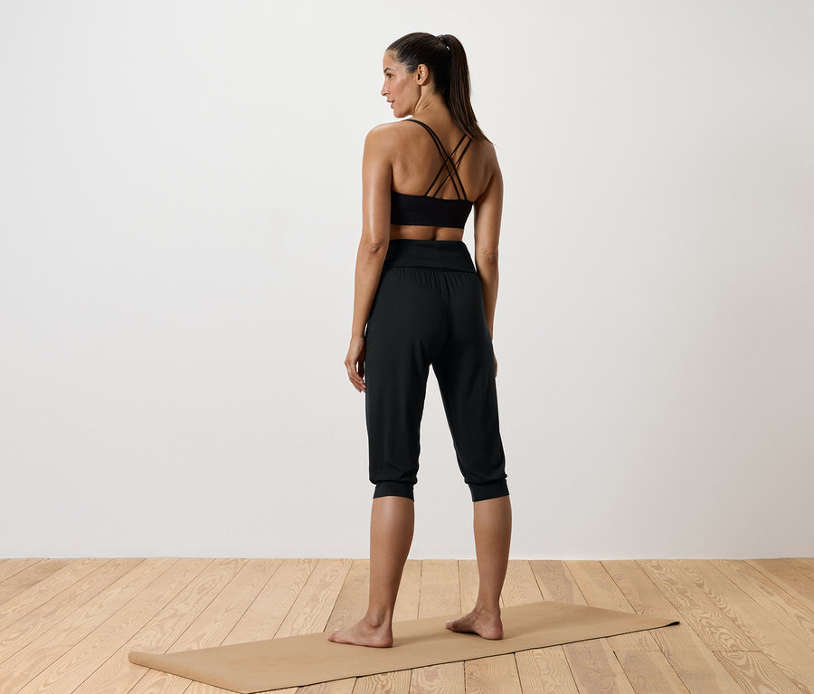 Une femme debout sur un tapis de yoga, portant un haut de sport noir et un pantalon noir.