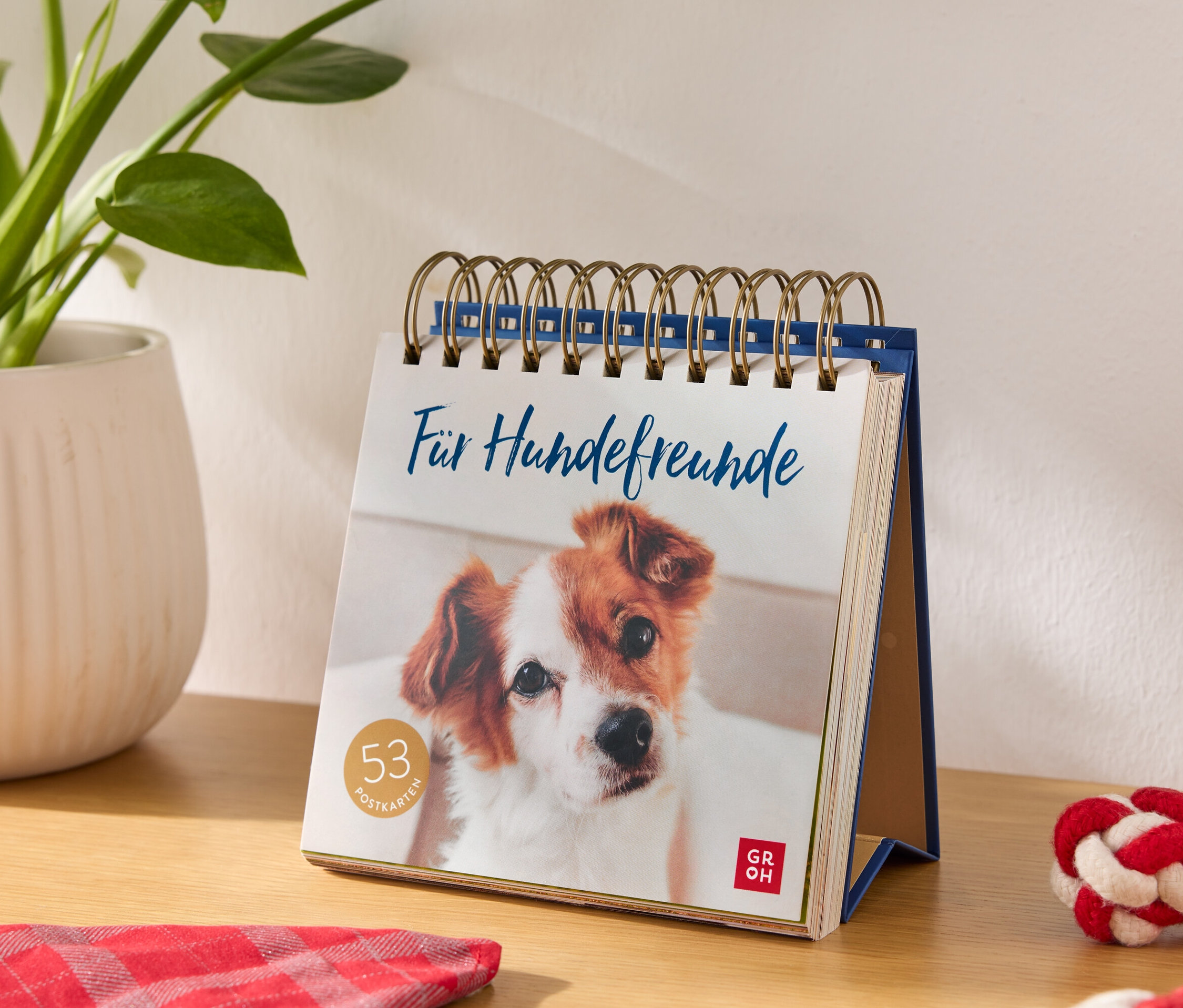 Calendrier de table avec l'inscription "Pour les amis des chiens" et une image de chien, à côté d'un pot de fleurs et d'un jouet pour chien.
